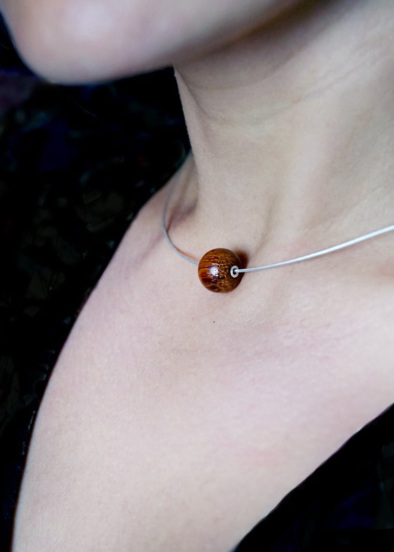 Close-up of a necklace with a brown wood bead and sterling silver detail on a dark background