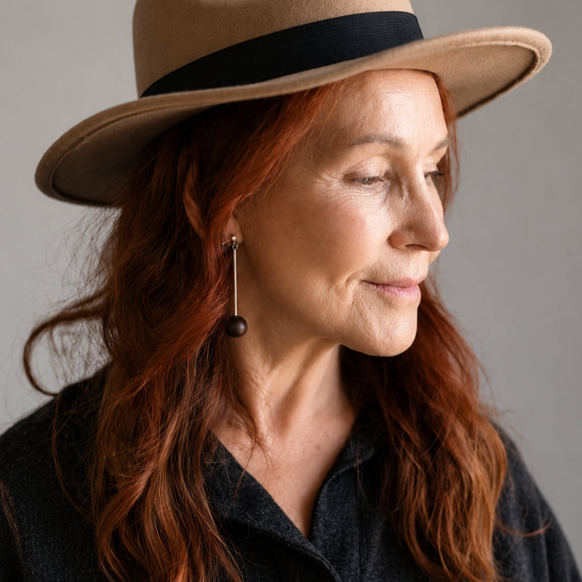 woman wearing hat with black wood bead drop earrings in silver over grey background