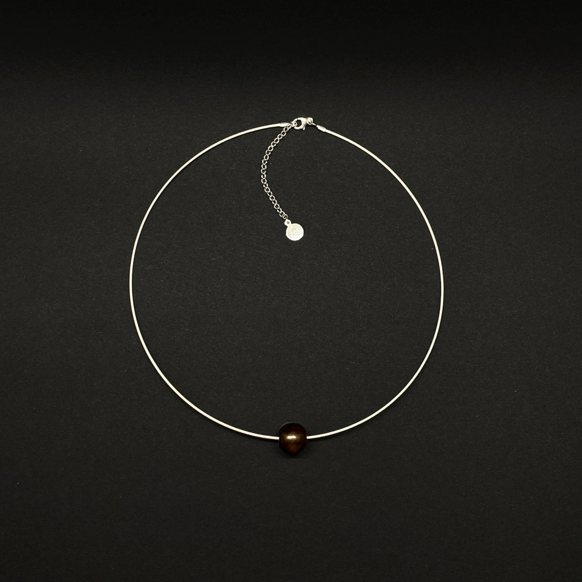 A delicate silver wire choker necklace featuring a single black wood bead at the bottom center, displayed on a dark black background.