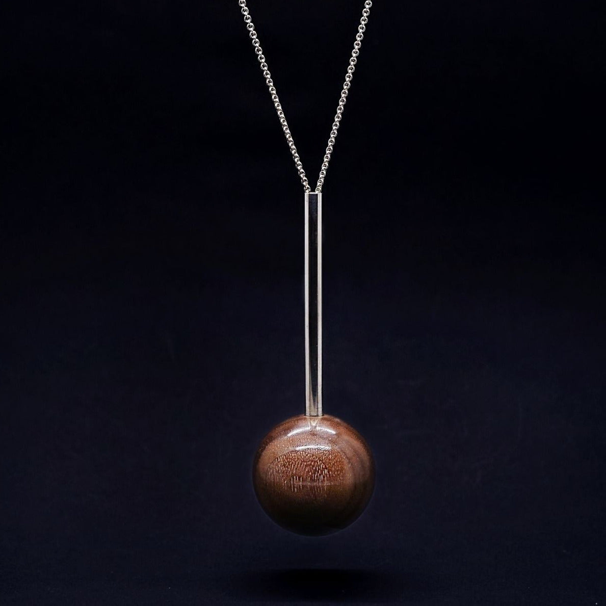 sterling silver tube and wood bead pendant on long silver chain necklace on black background