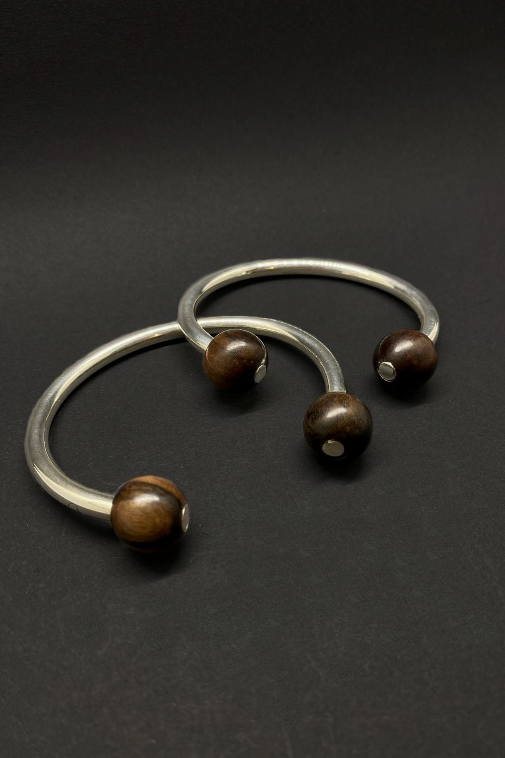 two silver bangles his and hers with brown beads on a dark background