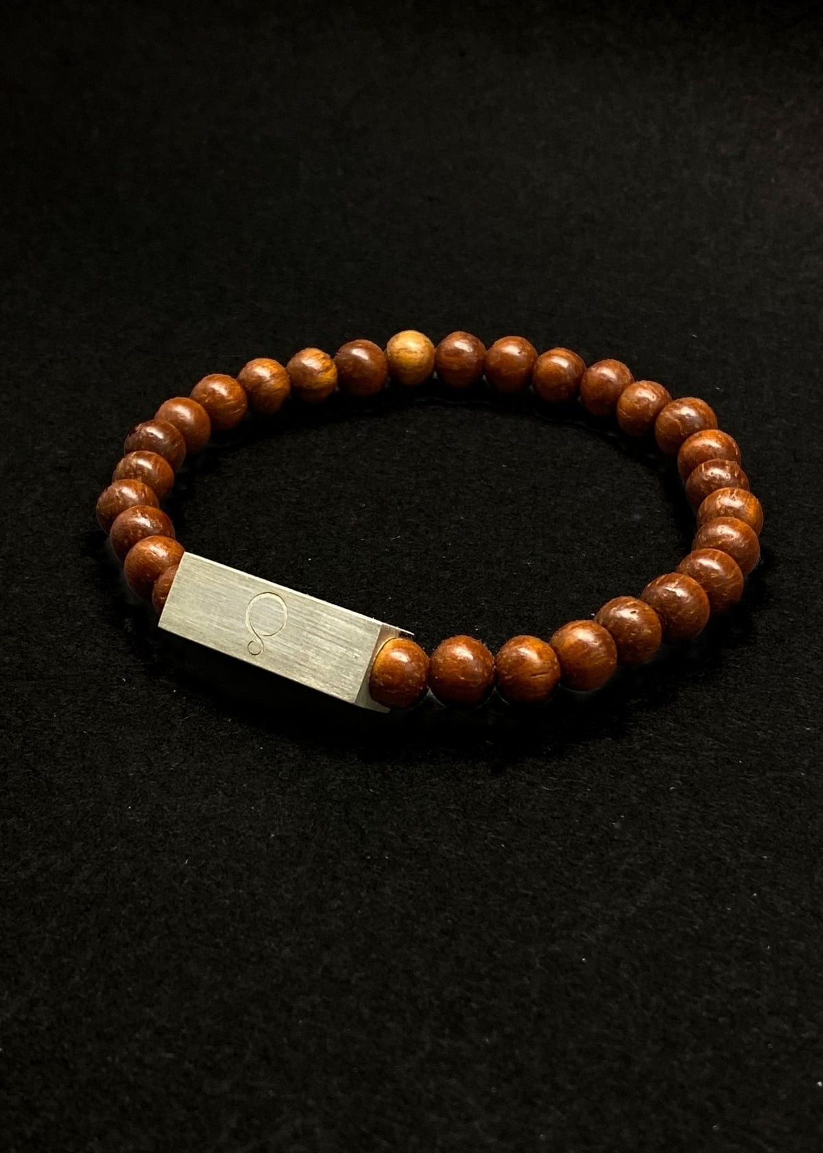Wooden beaded bracelet with a silver block on a black background