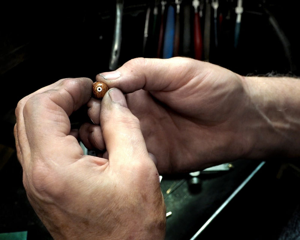 jewellers hands holding wood bead and silver detailing