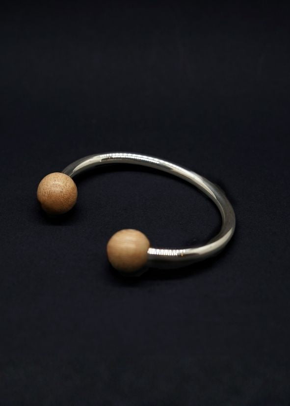 Silver bracelet with two beige beads on a black background