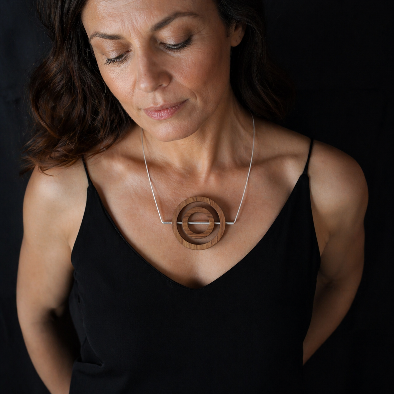 Woman wearing a black top with a wooden necklace against a dark background