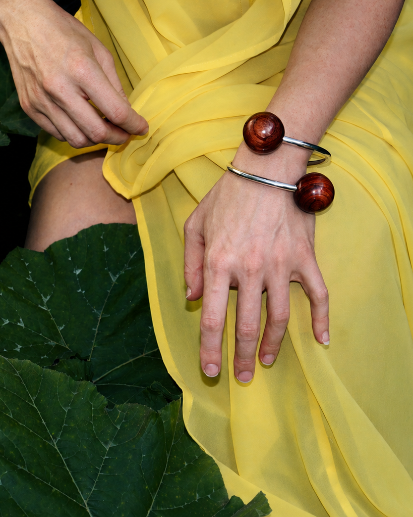 Person wearing a yellow dress with green leaves in the background with silver bracelet