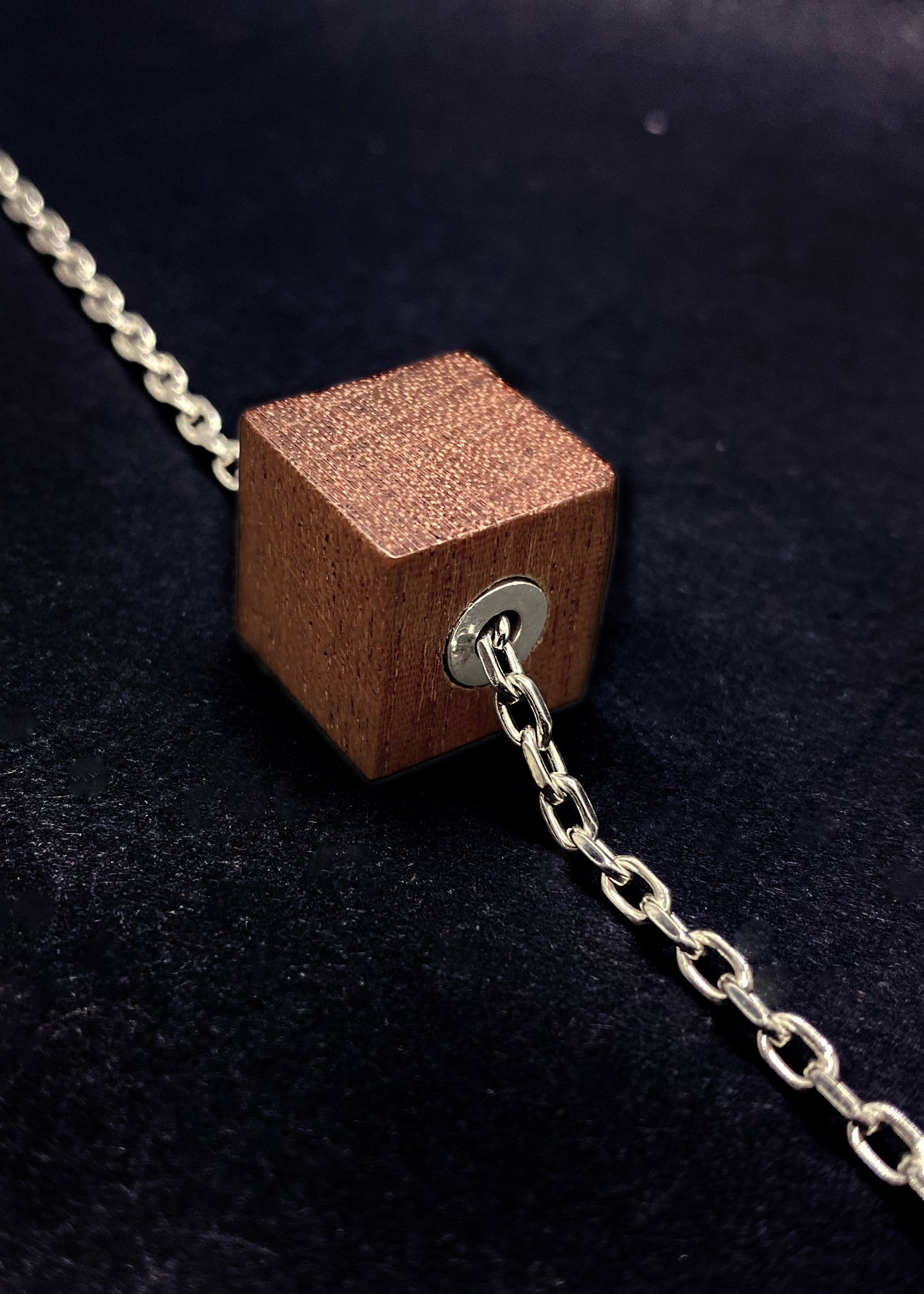 Wooden cube pendant on a chain against a dark background