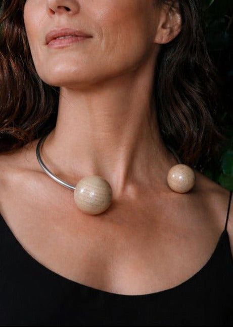 Woman wearing a necklace with large wood beads on silver against a green leafy background