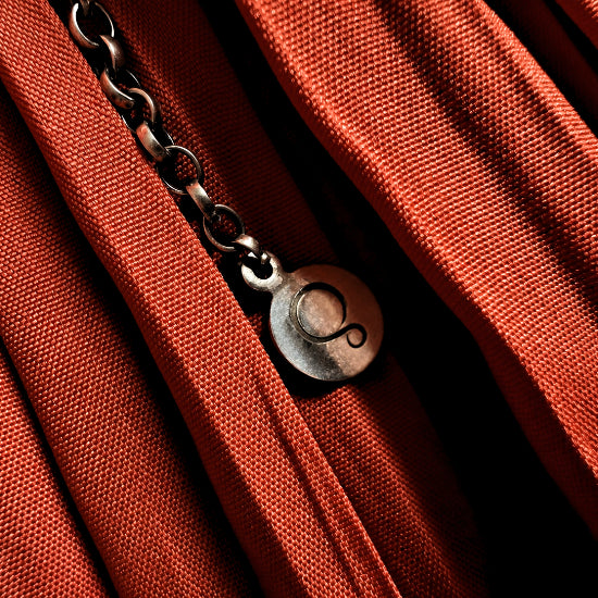 Close-up of a rust-orange woven fabric with a silver chain and round charm engraved with the silverwood logo.