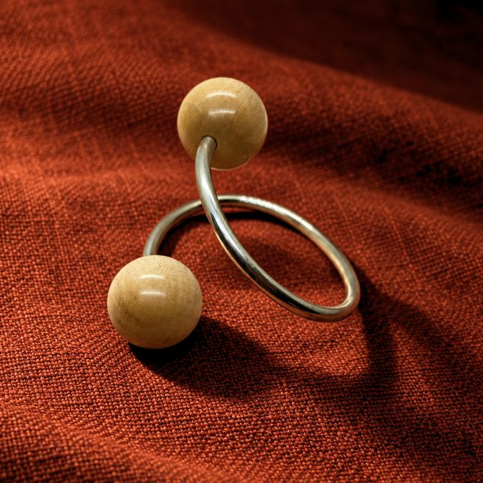 A sterling silver twisted torque bracelet featuring two spherical, light beige wooden beads suspended on the band, displayed on a textured rust-red fabric background.