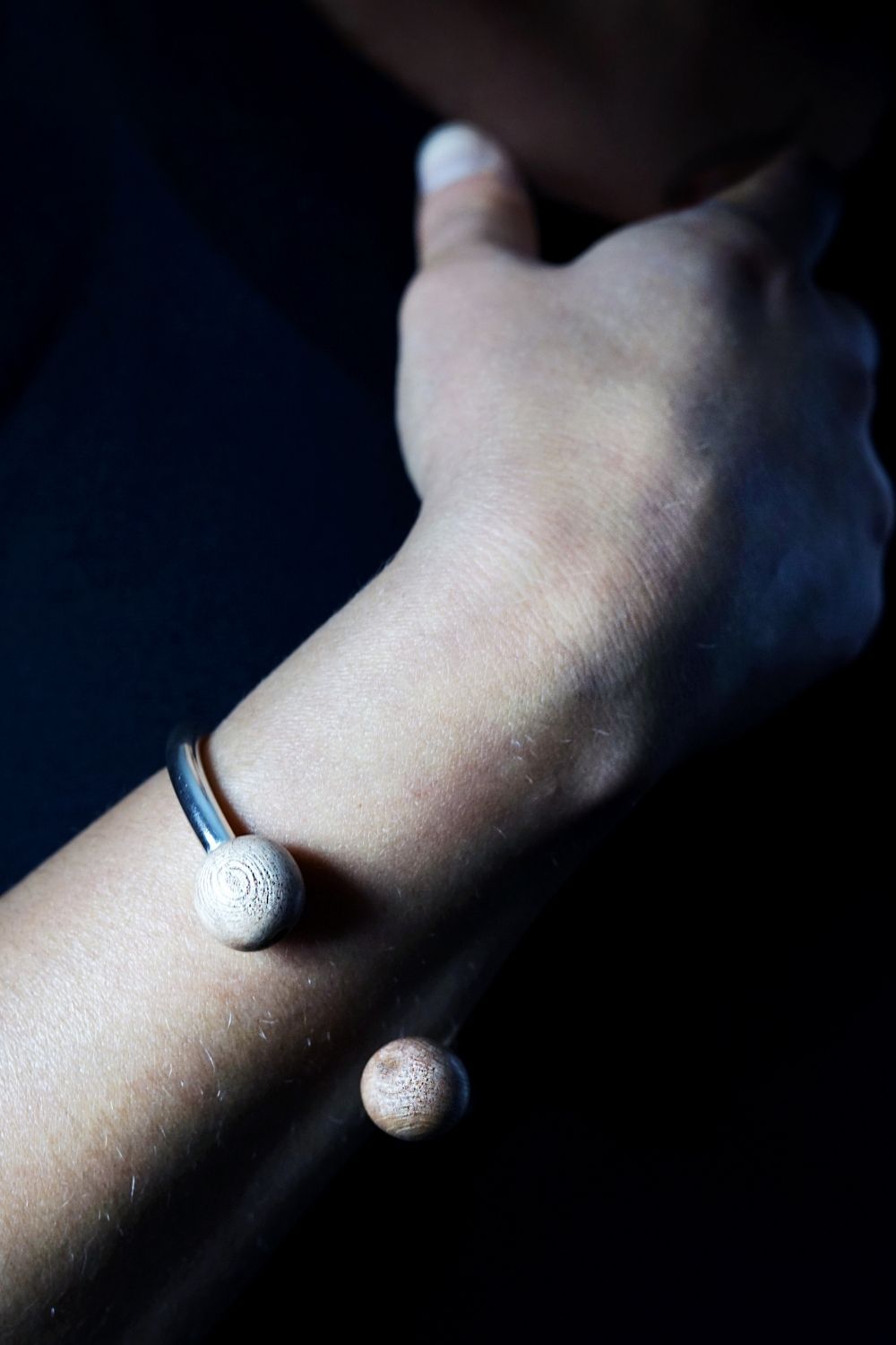 Close-up of a wrist wearing a silver bracelet with two round wood beads on a dark background