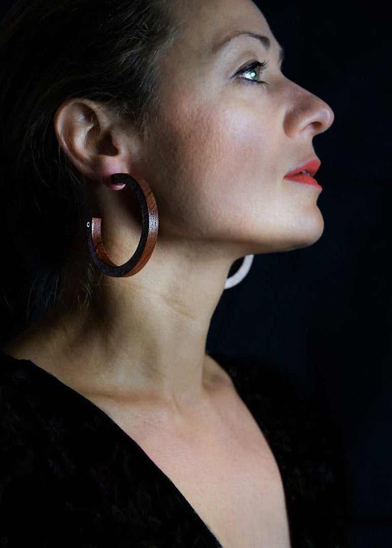 Woman wearing bubinga wood hoop earrings and a dark top against a black background