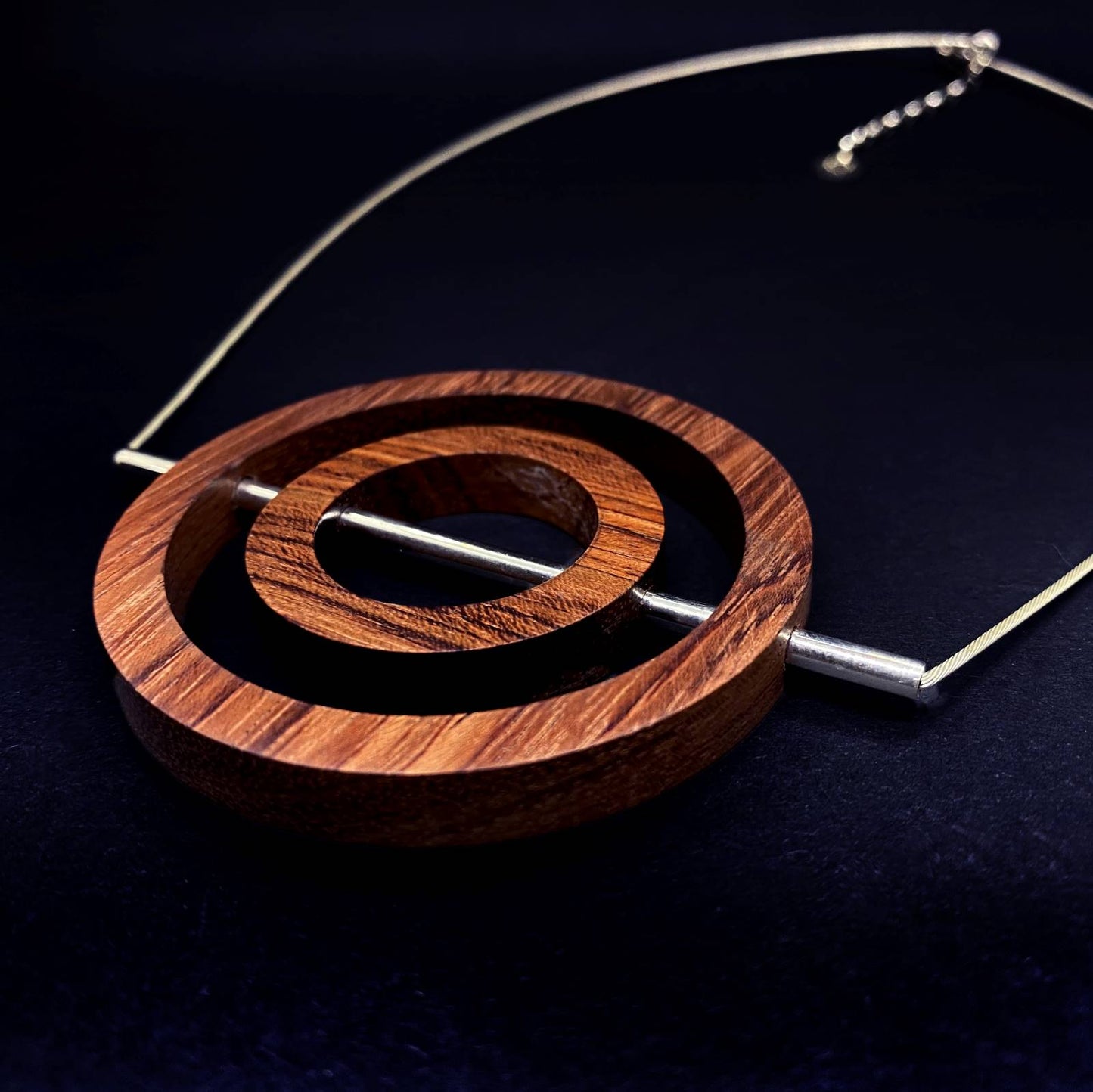 close view of the red wood concentric circle and silver tube pendant sitting on silver cable chain with extendor vegan handmade jewellery from Silverwood